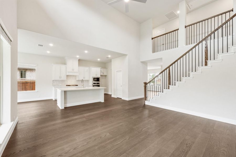 Open-concept living area with two-story ceiling, dark hardwood floors, white kitchen island, and staircase with iron balusters.