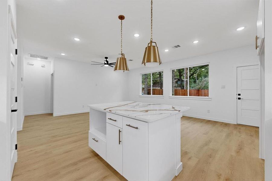 Kitchen featuring white cabinets, hanging light fixtures, light stone countertops, recessed lighting, and light wood-style floors Kitchen featuring white cabinets, hanging light fixtures, light stone countertops, recessed lighting, and light wood-style floors