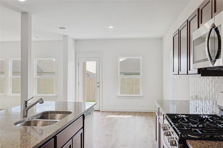 Kitchen featuring dark brown cabinetry, light stone countertops, sink, appliances with stainless steel finishes, and light wood-type flooring