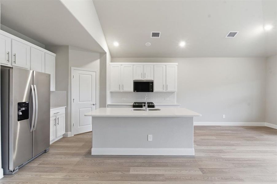 The kitchen features white shaker style cabinetry, a stainless steel refrigerator, and a kitchen island with a sink and faucet