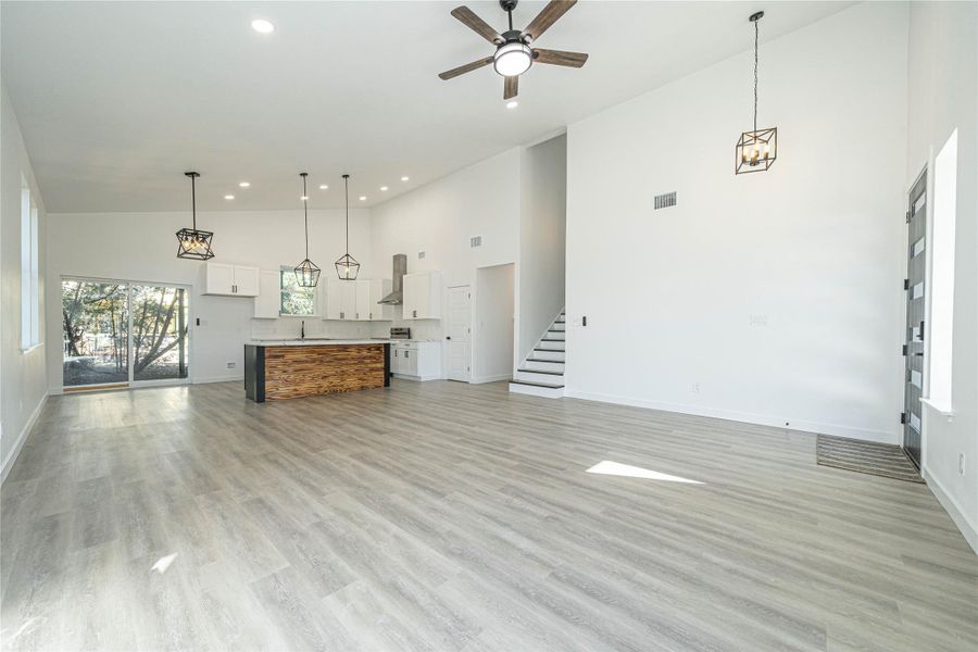 Unfurnished living room with high vaulted ceiling, stairs, light wood finished floors, recessed lighting, and ceiling fan