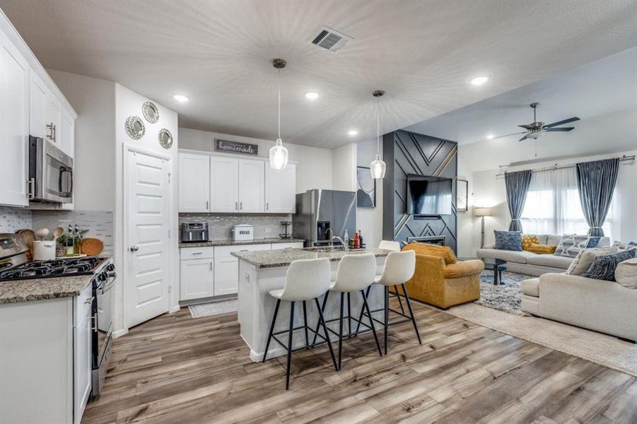Kitchen with open floor plan, appliances with stainless steel finishes, a breakfast bar, light stone countertops, and a center island with sink