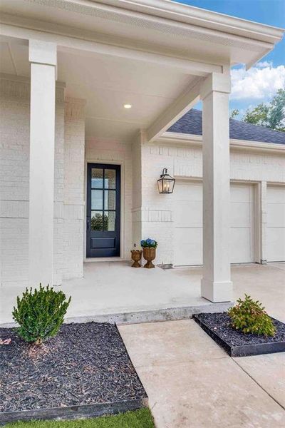 Property entrance with brick siding, a porch, concrete driveway, and an attached garage