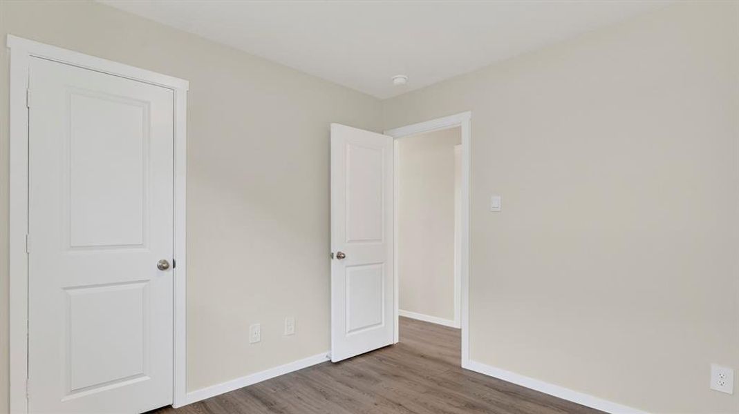 Interior room featuring two panel doors, wood-finish flooring, white baseboards, and light neutral wall paint