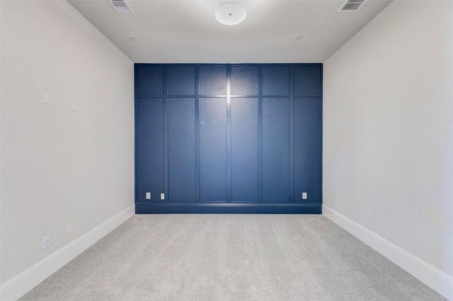 Media room features neutral carpet and light walls, complemented by a striking dark blue accent wall with paneling.