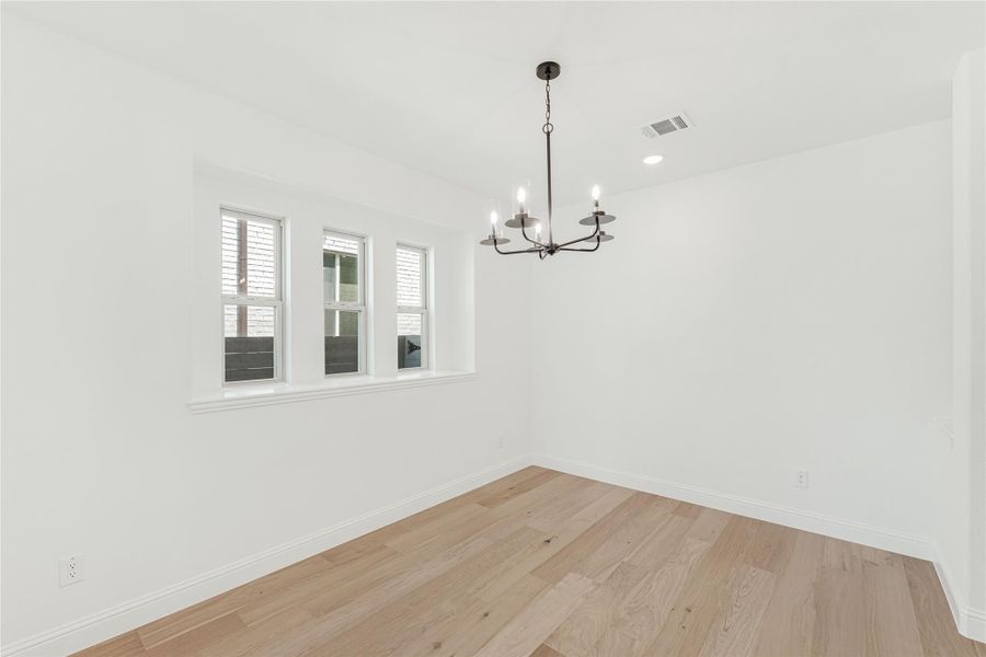 Empty dining room with light hardwood floors, white walls, and a black chandelier above three windows. Empty dining room with light hardwood floors, white walls, and a black chandelier above three windows.