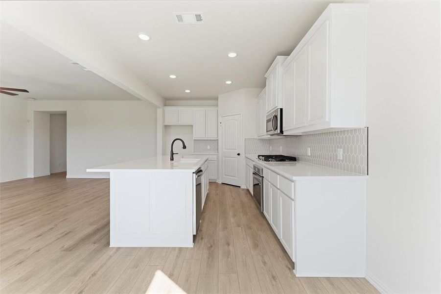 Kitchen with decorative backsplash, white cabinetry, recessed lighting, a kitchen island with sink, and light wood-style flooring