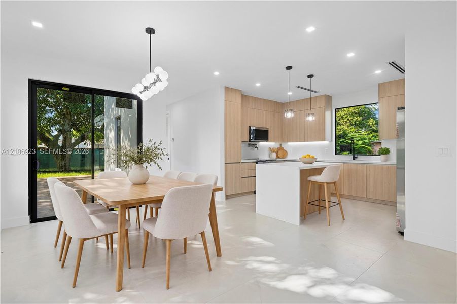 Modern kitchen featuring flat-panel wood cabinetry, a waterfall-edge center island with quartz countertops, recessed lighting, and large sliding glass doors providing outdoor access Modern kitchen featuring flat-panel wood cabinetry, a waterfall-edge center island with quartz countertops, recessed lighting, and large sliding glass doors providing outdoor access