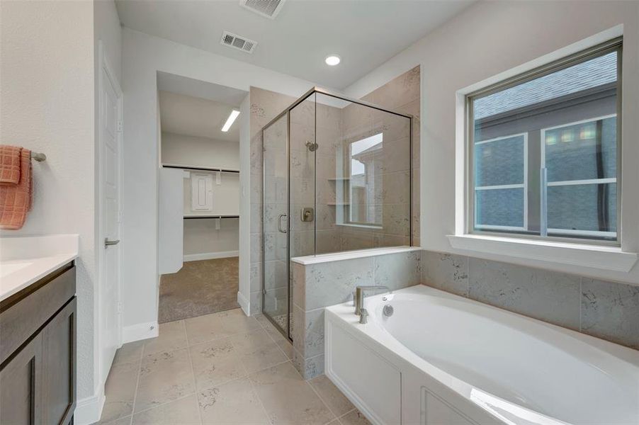 Full bathroom featuring a walk-in shower with clear glass enclosure, a white soaking tub, and a window above
