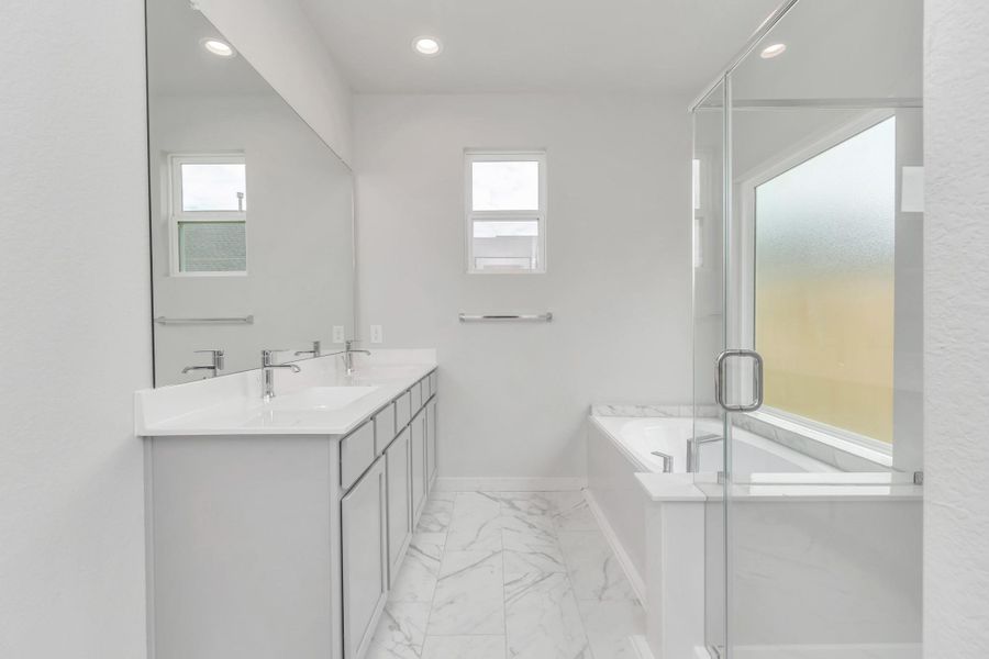 Escape to a spa-like oasis in this primary bathroom. Enjoy a walk-in shower with tile surround, a separate garden tub with custom detailing, and an elegant vanity featuring light countertops, modern hardware, and bright recessed lights. Experience luxury and relaxation in every detail. Sample photo of completed home with similar floor plan. Actual colors and selections may vary.