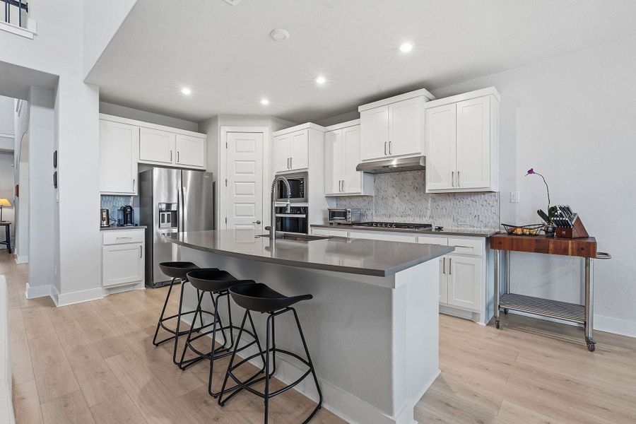 Kitchen with stainless steel appliances, tasteful backsplash, white cabinets, a breakfast bar area, and recessed lighting