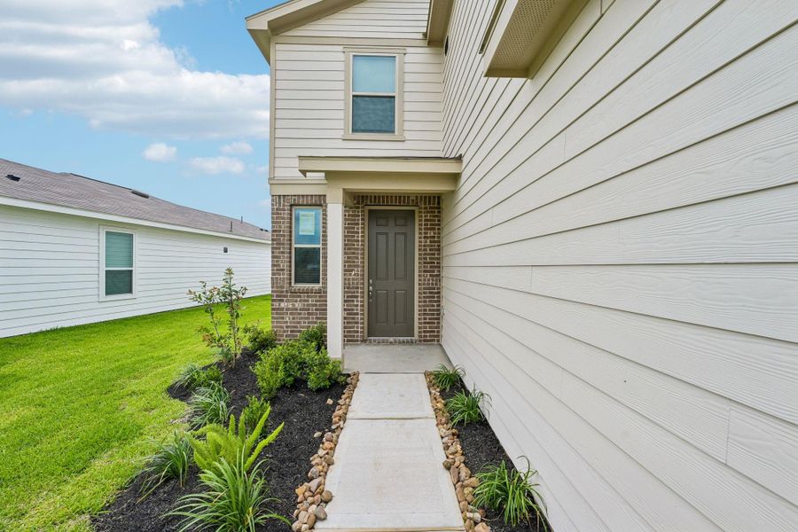 A welcoming covered entryway sets the tone with clean architectural lines and contrasting brick, a rich wood front door, and landscaped garden beds that create inviting curb appeal. A welcoming covered entryway sets the tone with clean architectural lines and contrasting brick, a rich wood front door, and landscaped garden beds that create inviting curb appeal.