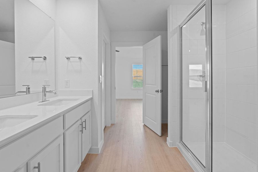 Full bath featuring double vanity, light wood-style flooring, and a stall shower