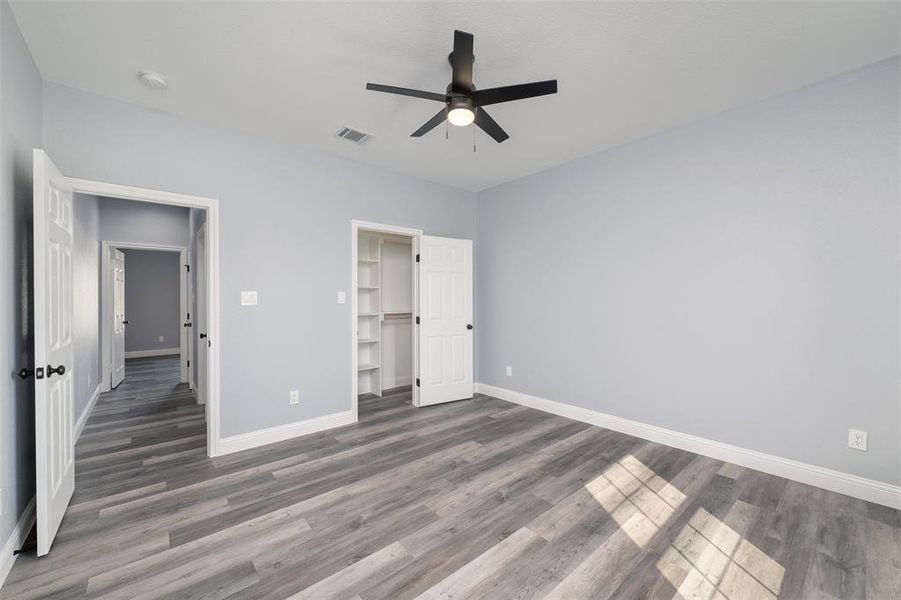 Unfurnished bedroom with wood finished floors, a ceiling fan, and a walk in closet Unfurnished bedroom with wood finished floors, a ceiling fan, and a walk in closet