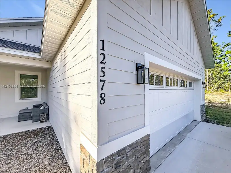 Exterior facade featuring horizontal lap siding, stone veneer accents, vertical paneling in the gable, and a paneled garage door with window inserts