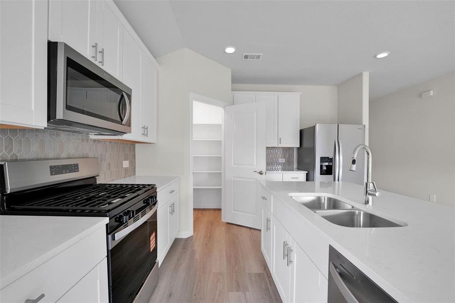 Kitchen with stainless steel appliances, decorative backsplash, white cabinets, light wood-type flooring, and light stone countertops Kitchen with stainless steel appliances, decorative backsplash, white cabinets, light wood-type flooring, and light stone countertops