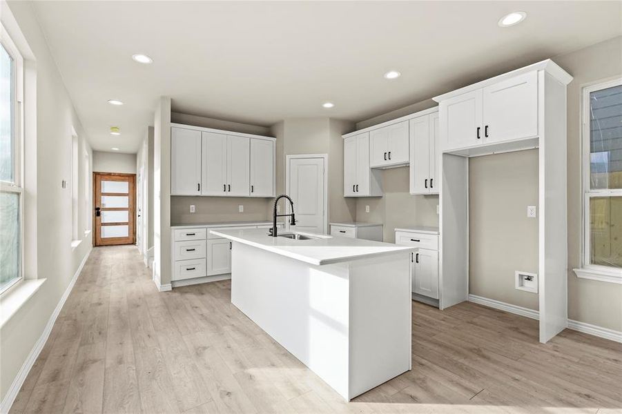 Kitchen with a healthy amount of sunlight, light hardwood / wood-style flooring, a center island with sink, and white cabinets