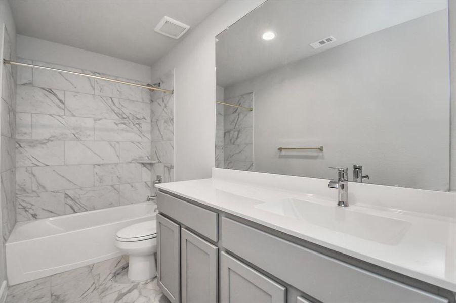 Sophistication within the secondary bathroom, where tile flooring perfectly complements a bath/shower combo surrounded by tile. Light wood cabinets, and a beautiful light countertop elevate the space, creating a truly inviting ambiance.