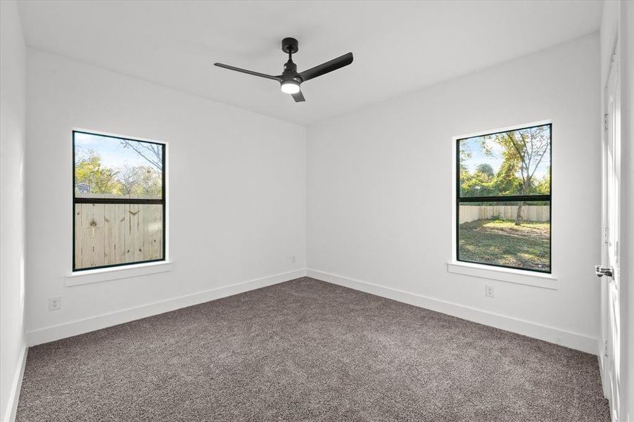 Empty room with carpet floors, a wealth of natural light, and ceiling fan