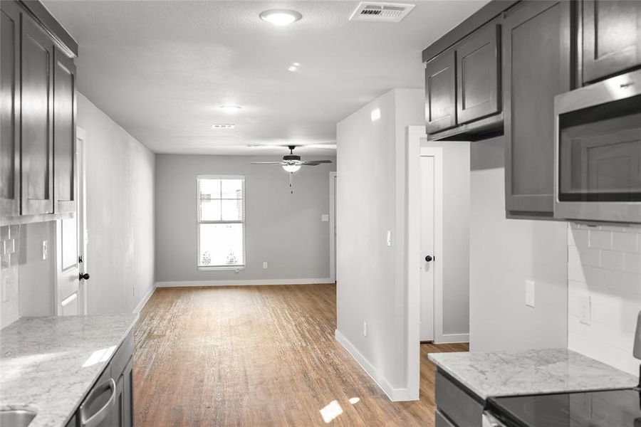 Kitchen featuring stainless steel microwave, range, light wood-style floors, a ceiling fan, and light stone counters