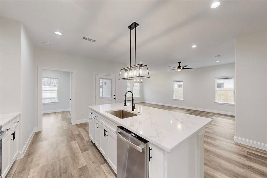 Kitchen with pendant lighting, white cabinetry, dishwasher, sink, and a kitchen island with sink