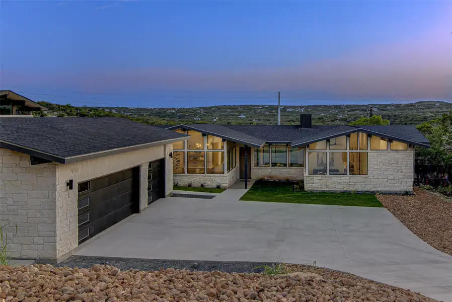View of front of property with stone siding, a sunroom, a shingled roof, and a detached garage View of front of property with stone siding, a sunroom, a shingled roof, and a detached garage