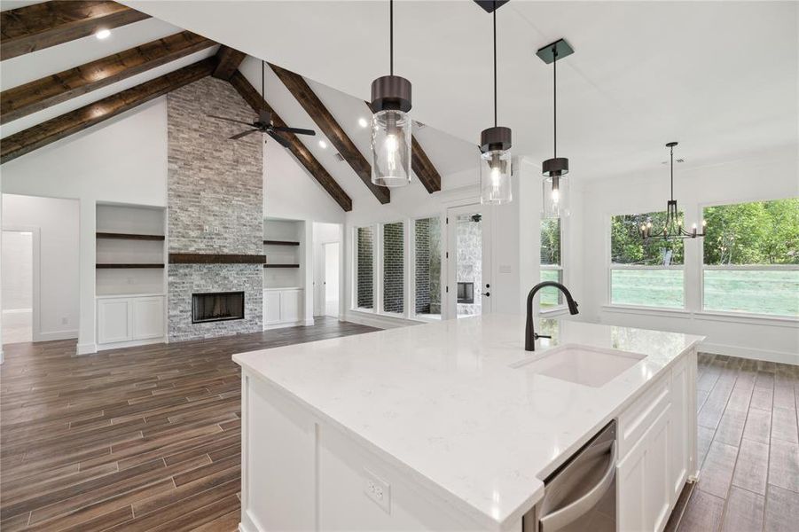 Kitchen featuring stainless steel dishwasher, built in shelves, sink, beam ceiling, and a kitchen island with sink