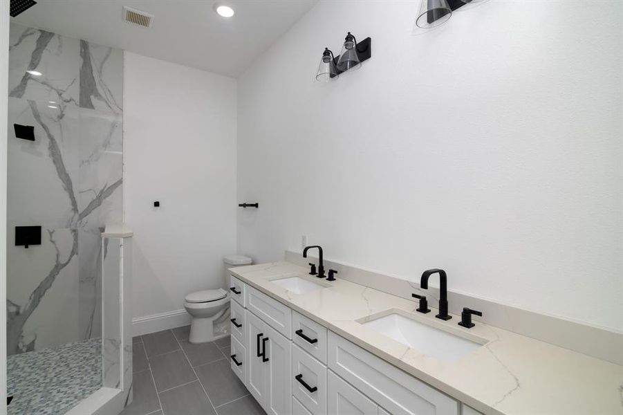 Bathroom featuring toilet, vanity, tile patterned flooring, and a tile shower