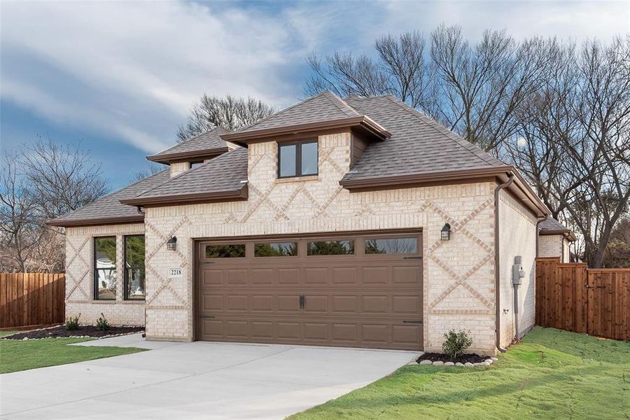 French country home featuring brick siding, a shingled roof, driveway, and an attached garage