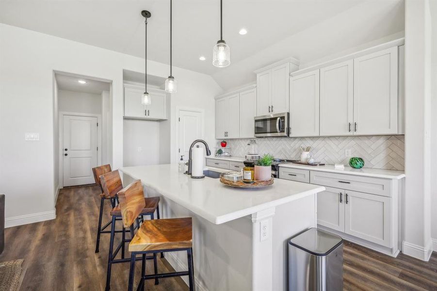 Kitchen with hanging light fixtures, dark hardwood / wood-style flooring, decorative backsplash, and an island with sink