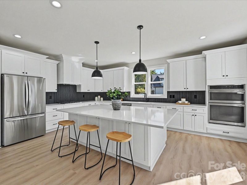 Bright designer kitchen features a large quartz island, stainless steel appliances, double ovens, abundant cabinetry, and an open-concept layout perfect for everyday living and entertaining.