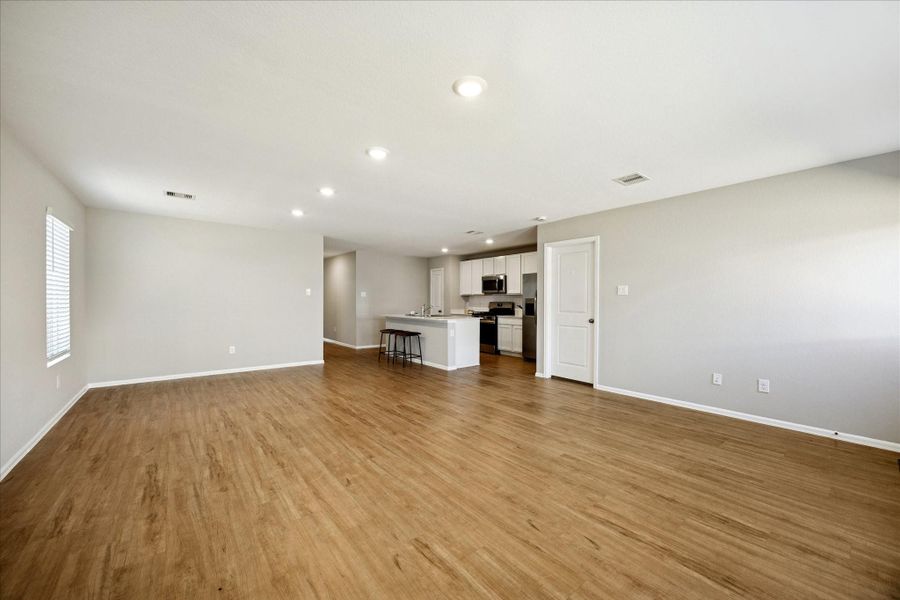 This spacious open-concept living area features viny flooring and neutral walls, seamlessly connecting to a modern kitchen with stainless steel appliances and a breakfast bar. Natural light enhances the inviting atmosphere.