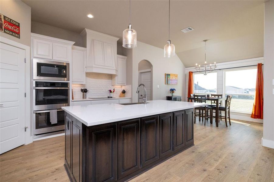 Kitchen with arched walkways, backsplash, pendant lighting, light wood-style flooring, and a chandelier