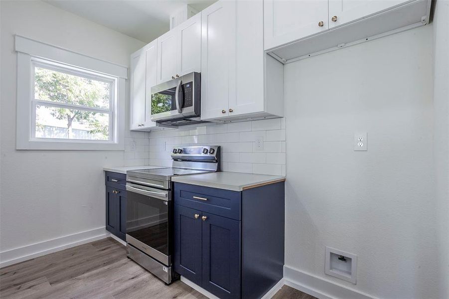 Modern kitchen featuring two-tone cabinetry with white upper and navy lower cabinets, stainless steel appliances, a white subway tile backsplash, and light wood-finish flooring