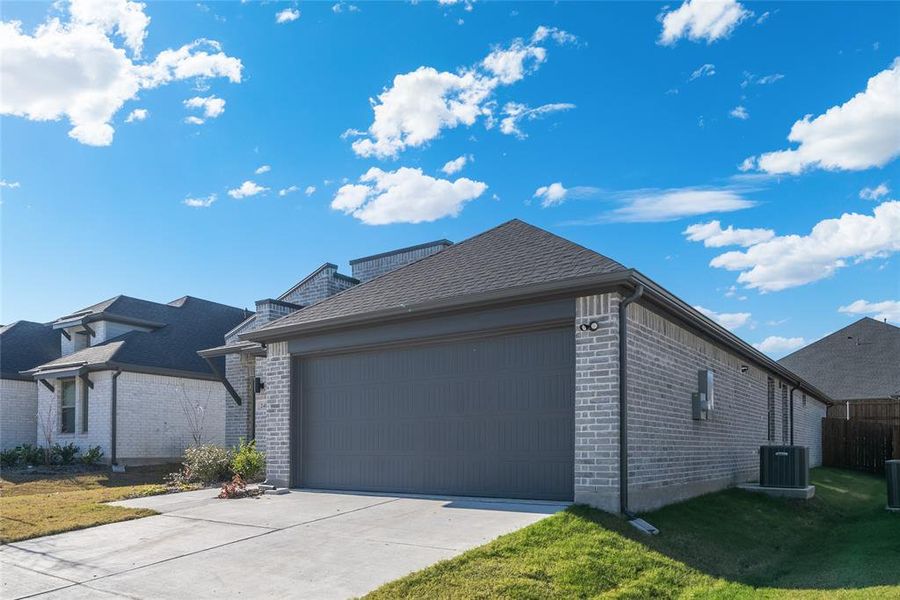 View of side of property featuring a lawn, central AC unit, and a garage