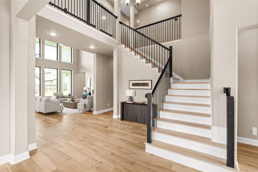 A grand open-concept living space with soaring ceilings, abundant natural light from large windows, and elegant hardwood floors, complemented by a modern staircase leading to the upper level. *Virtually Staged*