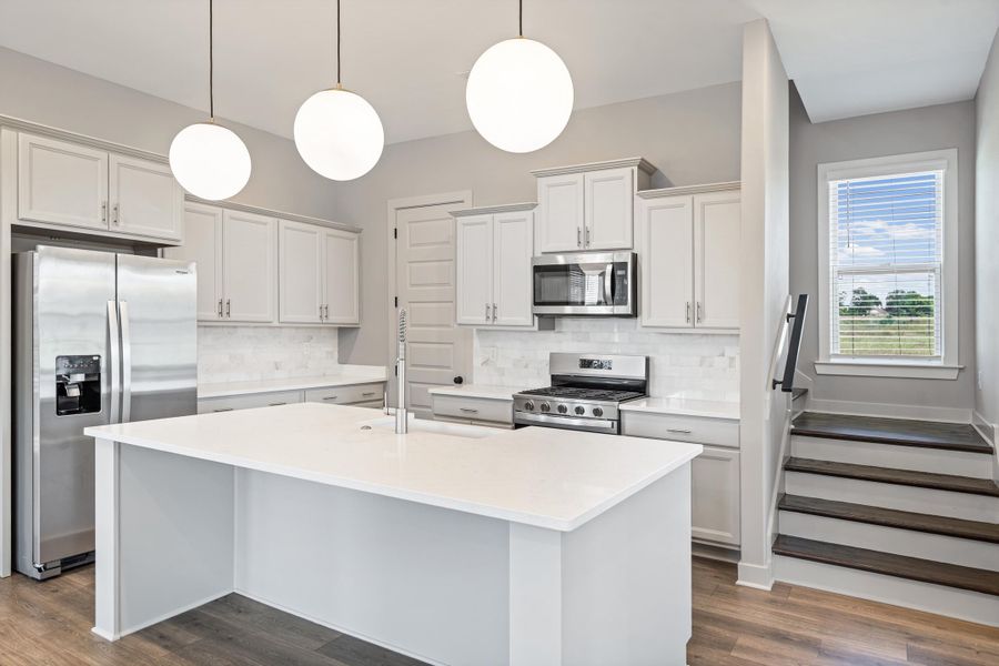 Kitchen featuring a central island with a solid surface countertop, stainless steel appliances, light cabinetry, and wood-finish flooring
