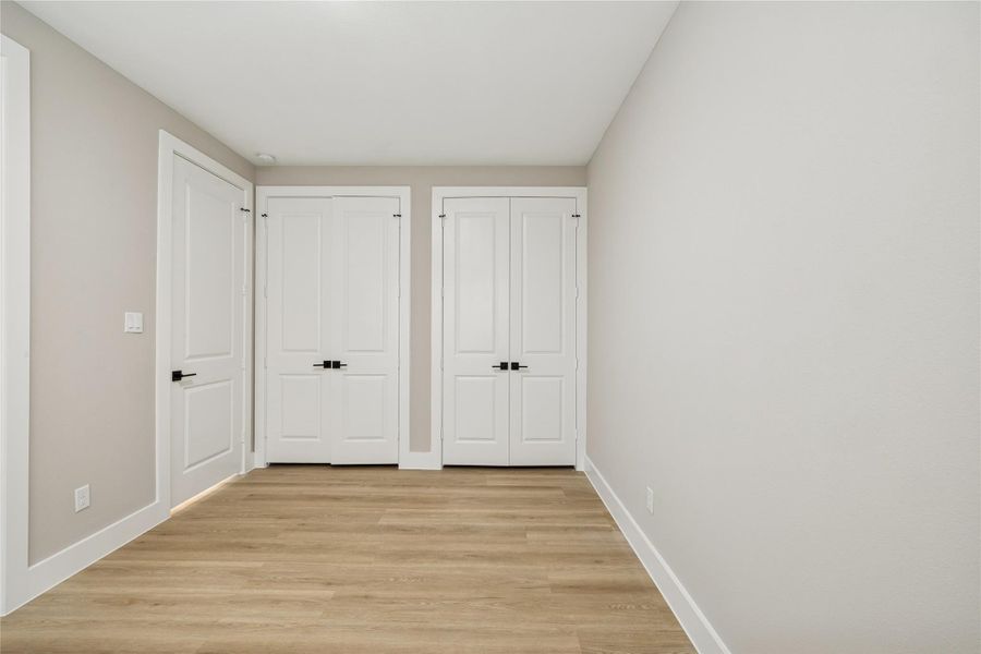 This room features a clean, modern design with light wood flooring and neutral walls. It includes two white double doors, providing ample closet space or entry to an adjoining room. Bright and minimalist, perfect for customization.