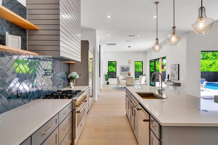 Kitchen with gray cabinetry, stainless steel appliances, light stone countertops, a kitchen island with sink, and pendant lighting