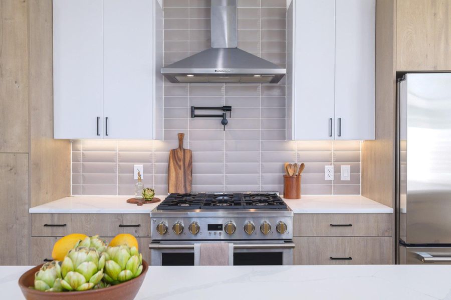 Two tone kitchen with stainless steel appliances, light stone counters, decorative backsplash, and dual tone cabinetry