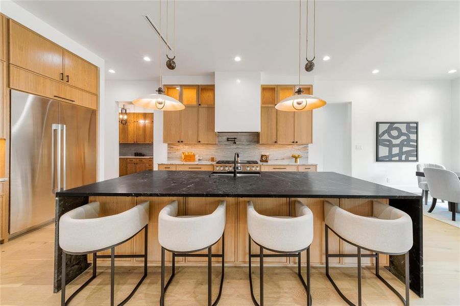 Kitchen with a kitchen bar, built in refrigerator, dark stone countertops, and a large island with sink