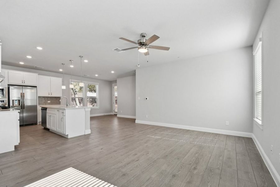Image of a living and dining room with an open kitchen, light grey walls, a ceiling fan, and white trim