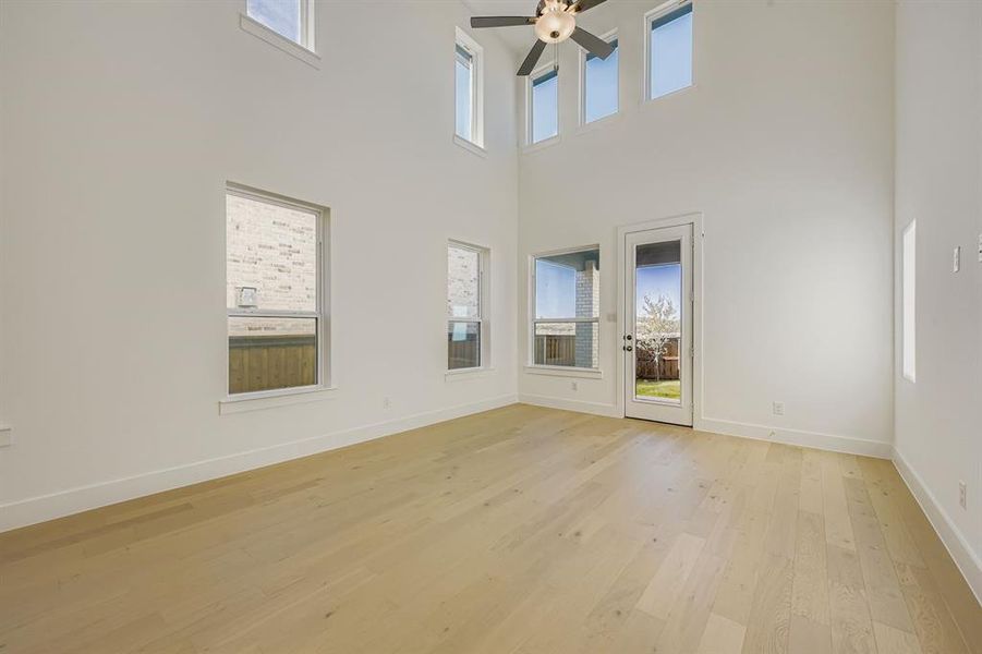 Spare room featuring light wood finished floors, a towering ceiling, and a ceiling fan