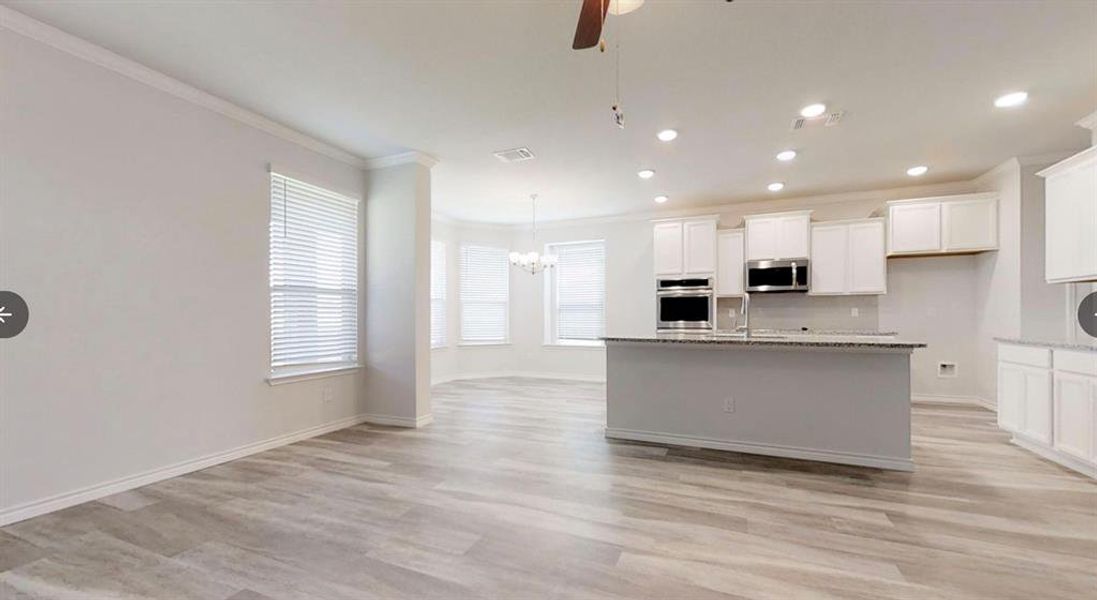 Kitchen featuring stainless steel appliances, crown molding, light wood finished floors, an island with sink, and white cabinetry