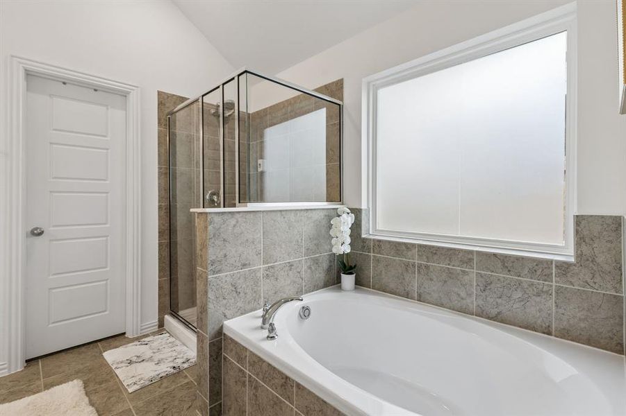 Soaking tub with a tiled surround, framed by a large privacy window
