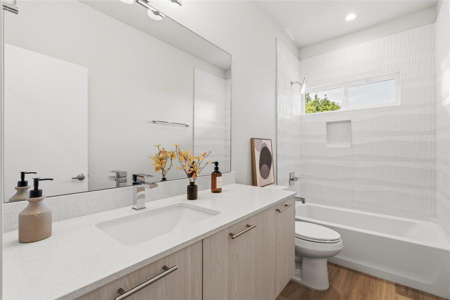 A well-appointed full bath serving both secondary bedrooms, featuring a quartz vanity, modern cabinetry, and a tiled tub surround with a built-in niche and natural light.
