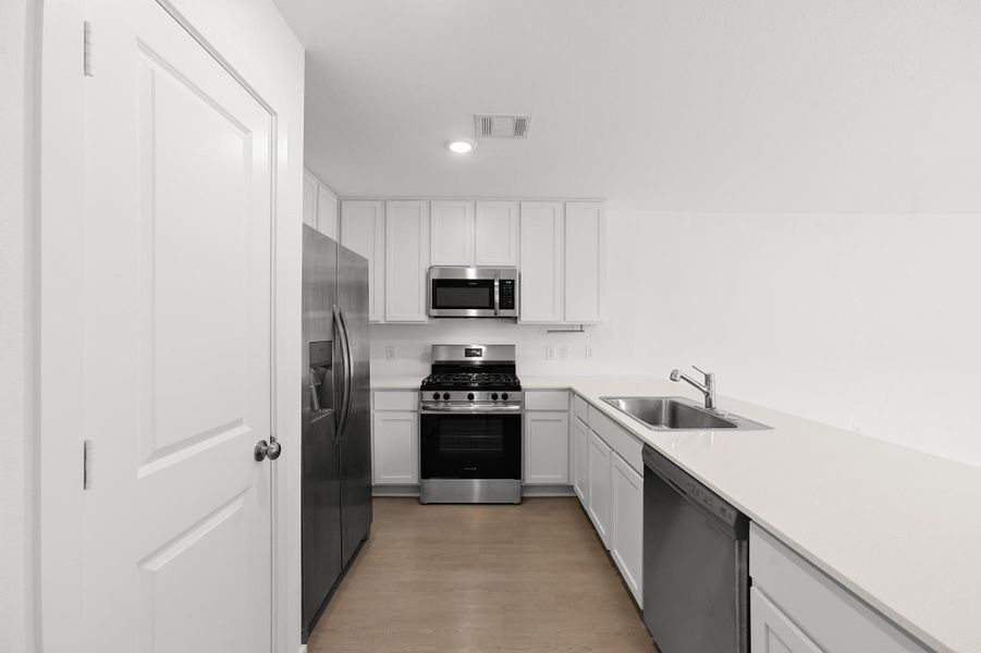 Another view highlights the kitchen’s efficient layout with white cabinetry, stainless steel appliances, recessed lighting, and ample countertop workspace. Another view highlights the kitchen’s efficient layout with white cabinetry, stainless steel appliances, recessed lighting, and ample countertop workspace.