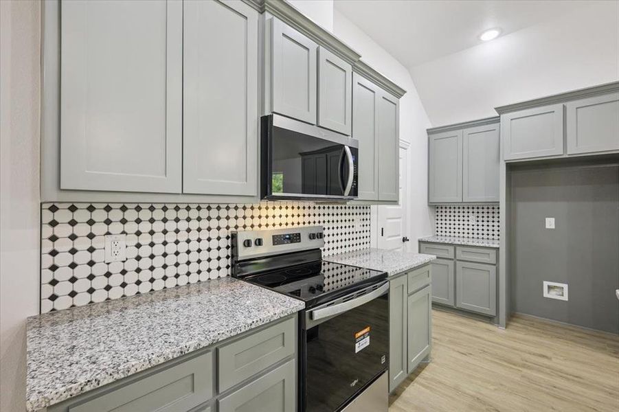 Kitchen featuring gray cabinets, appliances with stainless steel finishes, decorative backsplash, light stone counters, and vaulted ceiling Kitchen featuring gray cabinets, appliances with stainless steel finishes, decorative backsplash, light stone counters, and vaulted ceiling