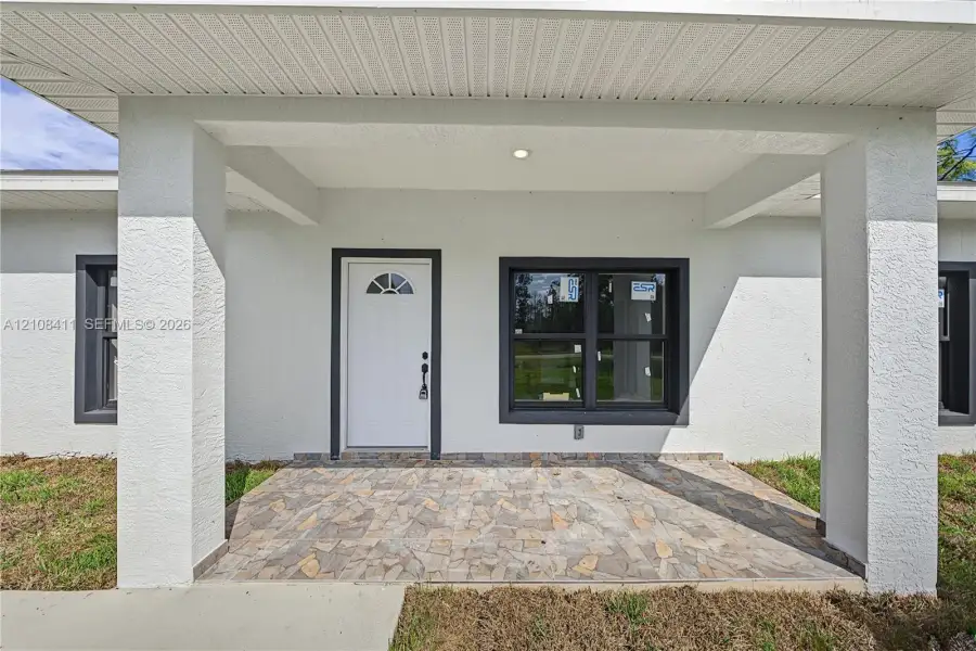 Covered entryway featuring a stone-paver porch, structural support columns, white door with a semi-circular transom window, and dark-framed windows