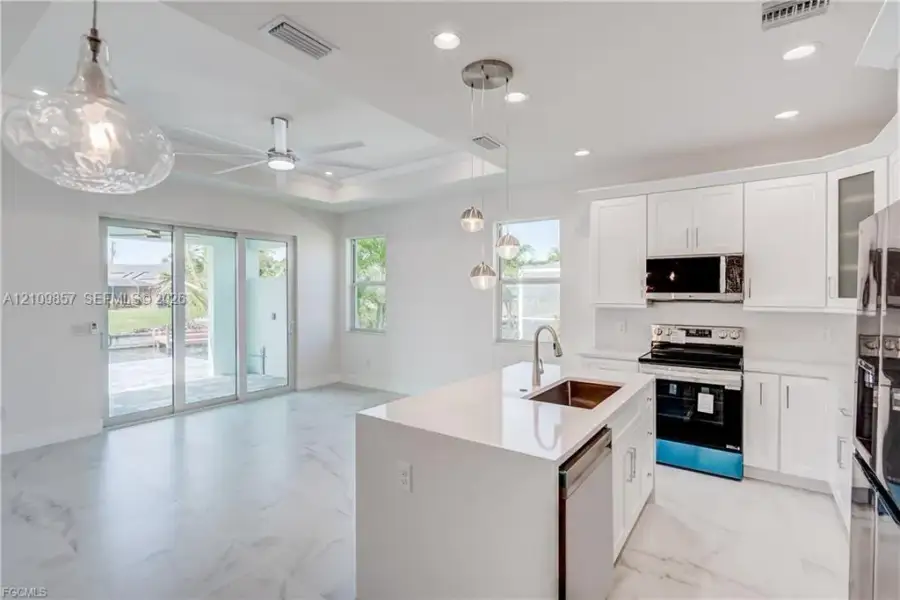 Kitchen featuring white shaker-style cabinetry, quartz countertops, a central island with a stainless steel undermount sink, recessed lighting, and large-format tile flooring